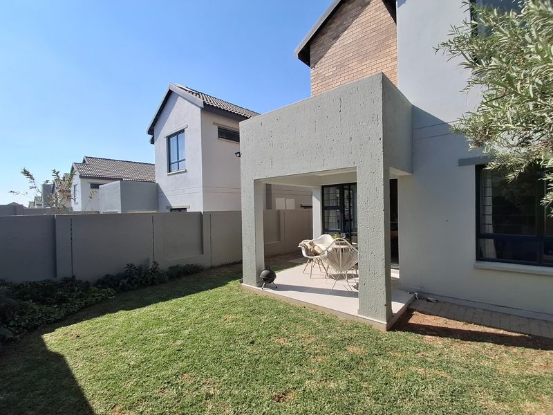 A well-maintained rear exterior view featuring a covered patio area, a private lawn, and secure boundary walling in a modern residential estate.