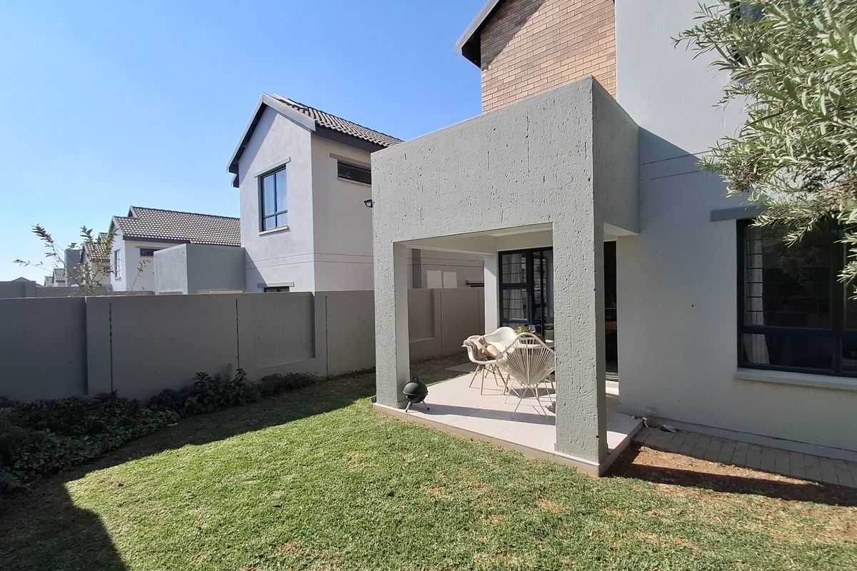 A well-maintained rear exterior view featuring a covered patio area, a private lawn, and secure boundary walling in a modern residential estate.