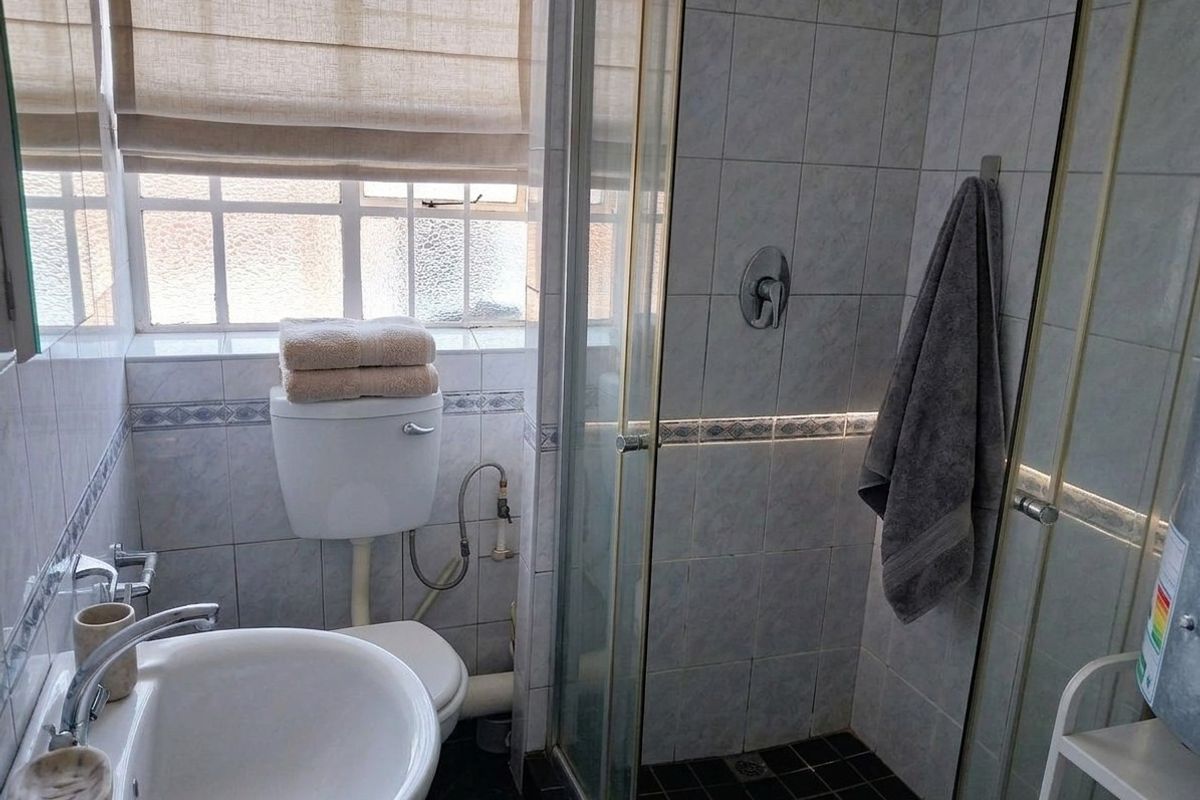 A functional bathroom featuring a shower enclosure, pedestal basin, and toilet with tiled finishes and natural light from a window.
