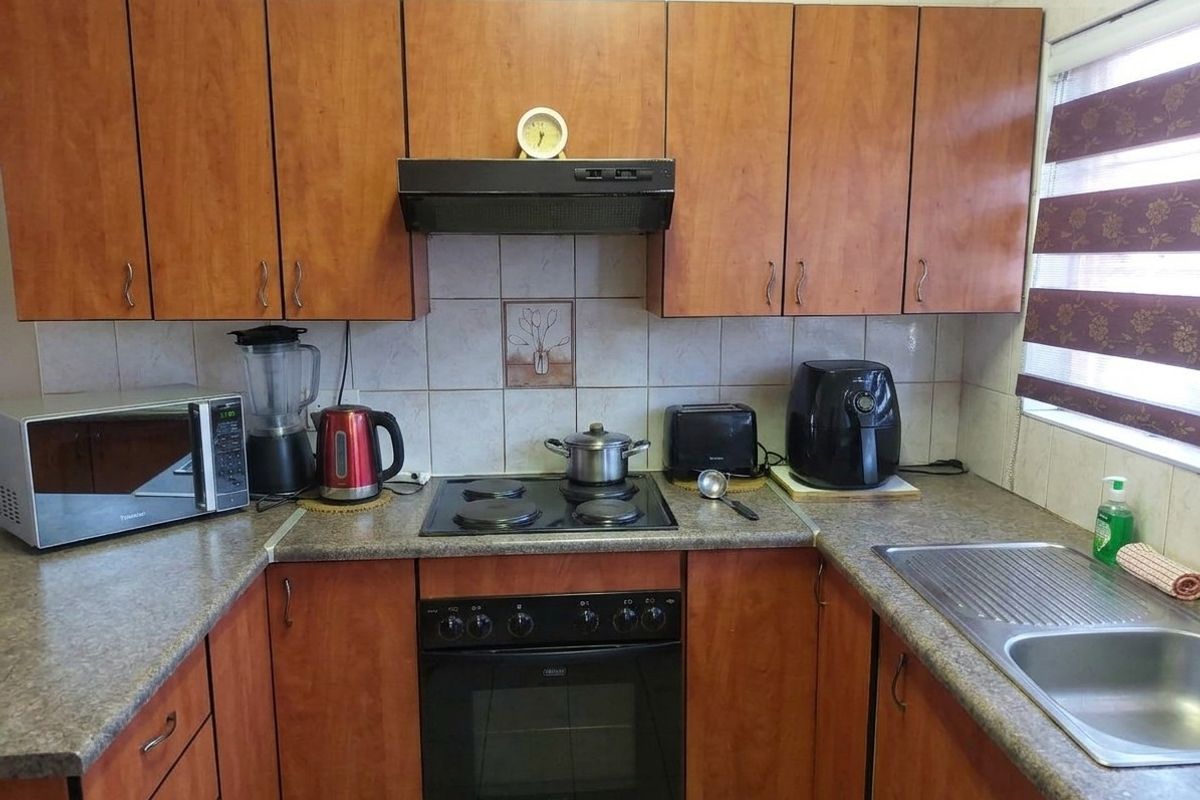 A functional kitchen featuring wood-look laminate cabinetry, dark countertops, a built-in oven with electric hob, and a stainless steel sink.