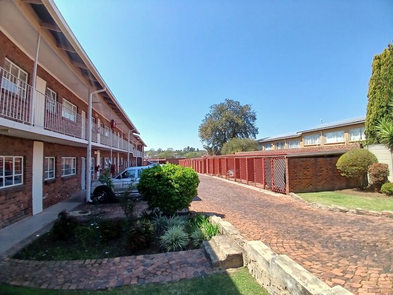 Exterior view of an apartment complex featuring brick facade, metal balcony railings, paved driveway, and a row of metal garage enclosures.