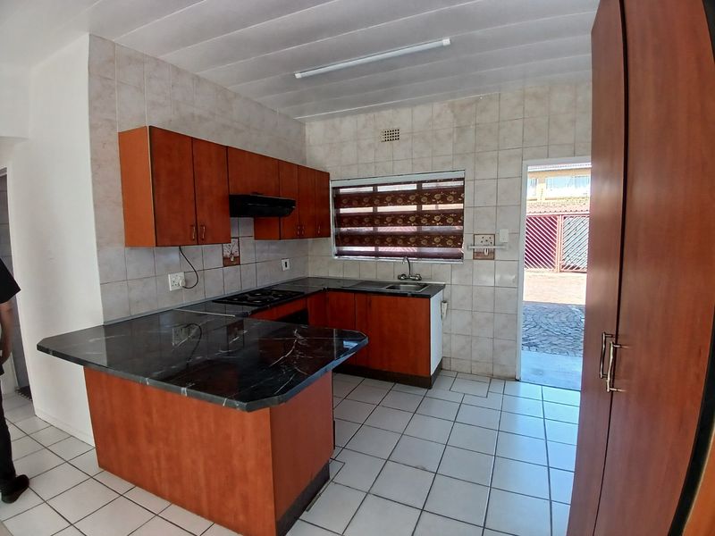 A functional kitchen featuring laminate cabinetry, a built-in hob with extractor, and tiled finishes, offering a practical layout with direct access to the exterior.