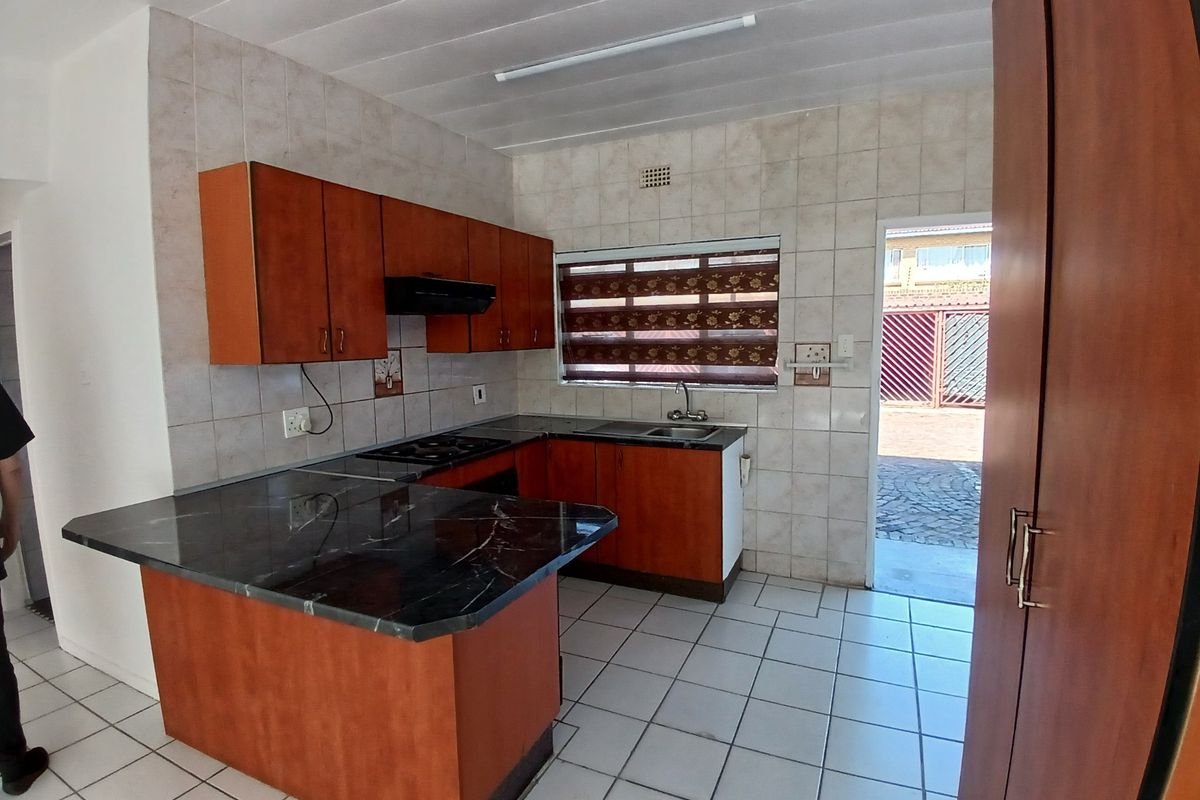 A functional kitchen featuring laminate cabinetry, a built-in hob with extractor, and tiled finishes, offering a practical layout with direct access to the exterior.