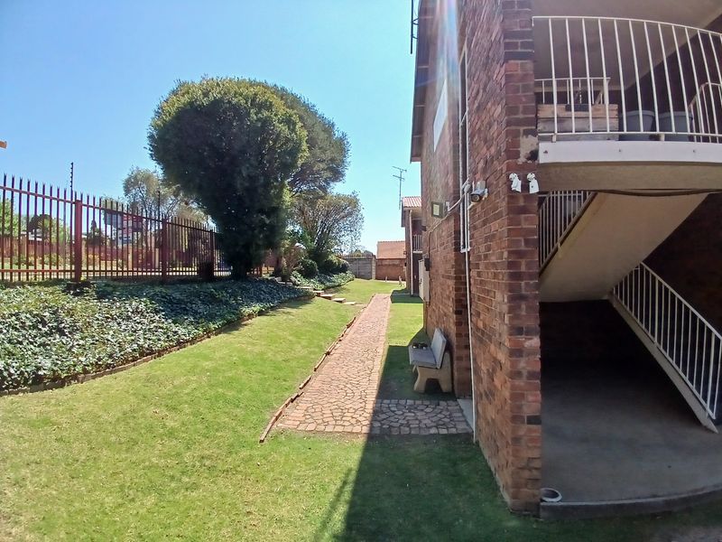 Exterior view of an apartment building featuring a brick facade, paved garden path, and external staircase with metal railings.