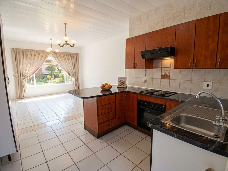 Open-plan kitchen and living area featuring wood-finish cabinetry, dark countertops, tiled flooring, and a bright, airy layout with garden views.