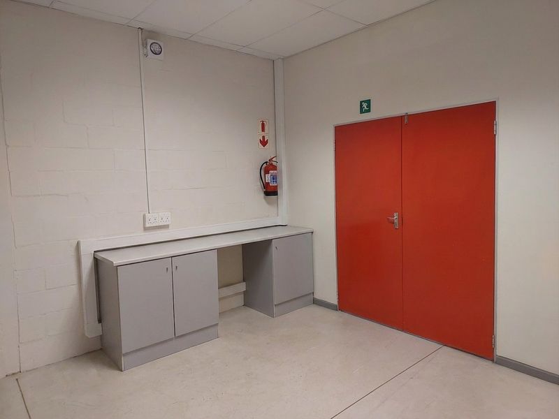 A functional office space featuring built-in cabinetry, a fire extinguisher, and a prominent red emergency exit door.
