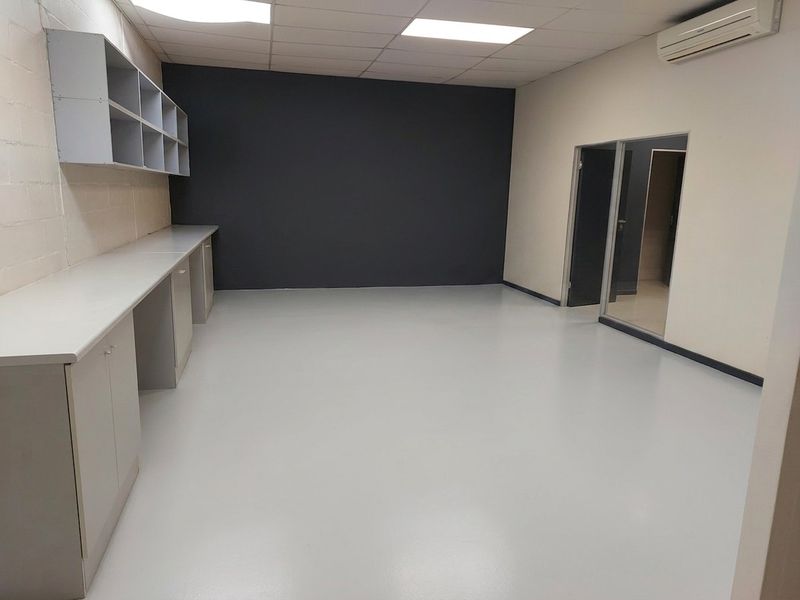 A clean, empty office space featuring durable epoxy flooring, built-in cabinetry, wall-mounted shelving, and a split-system air conditioning unit.