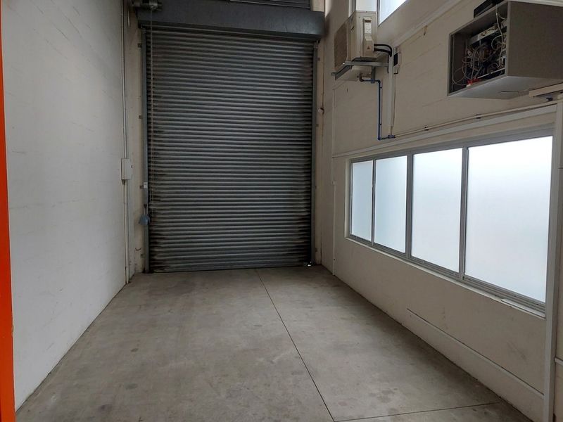 Empty industrial-style garage space featuring a large roller shutter door, concrete flooring, frosted windows, and an integrated air conditioning unit.