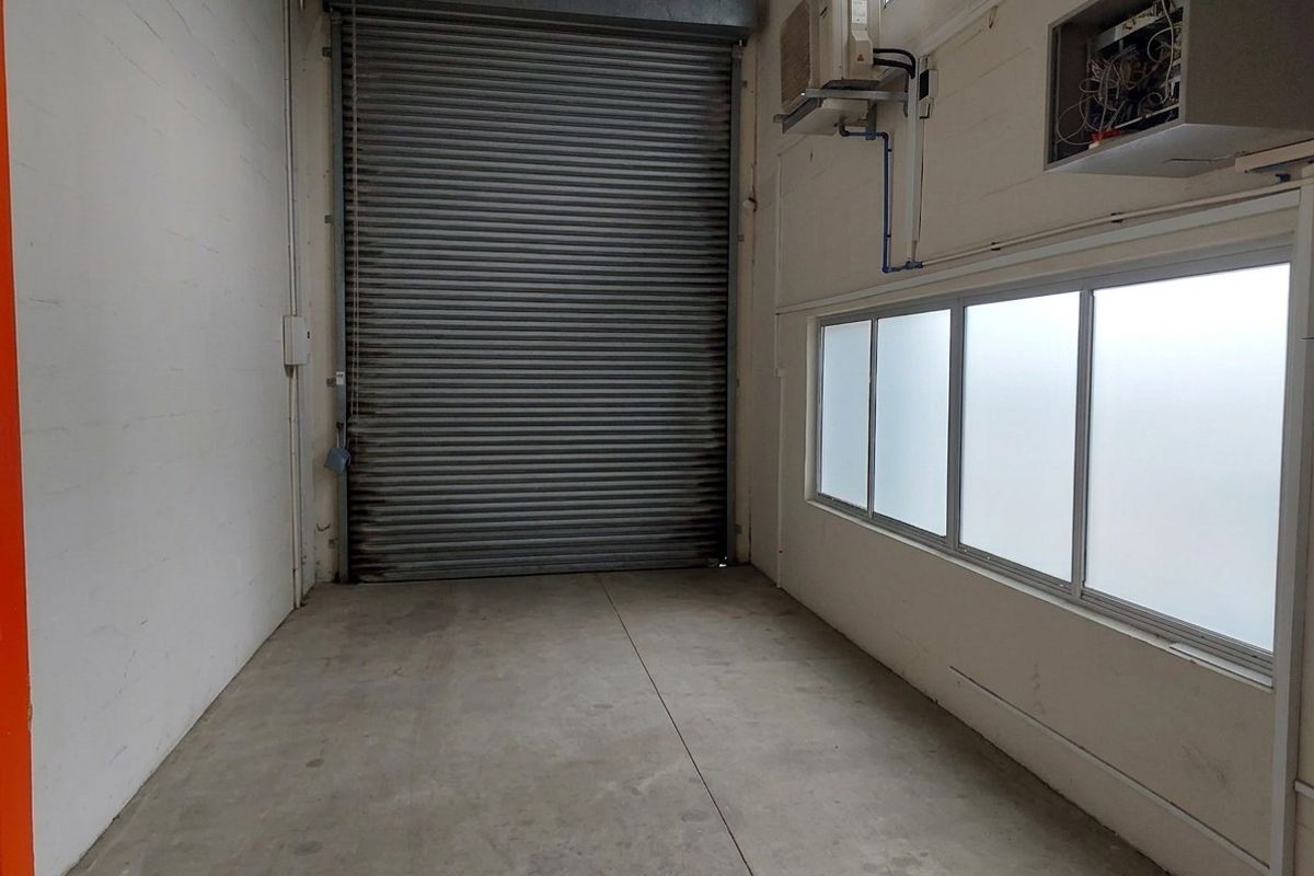 Empty industrial-style garage space featuring a large roller shutter door, concrete flooring, frosted windows, and an integrated air conditioning unit.