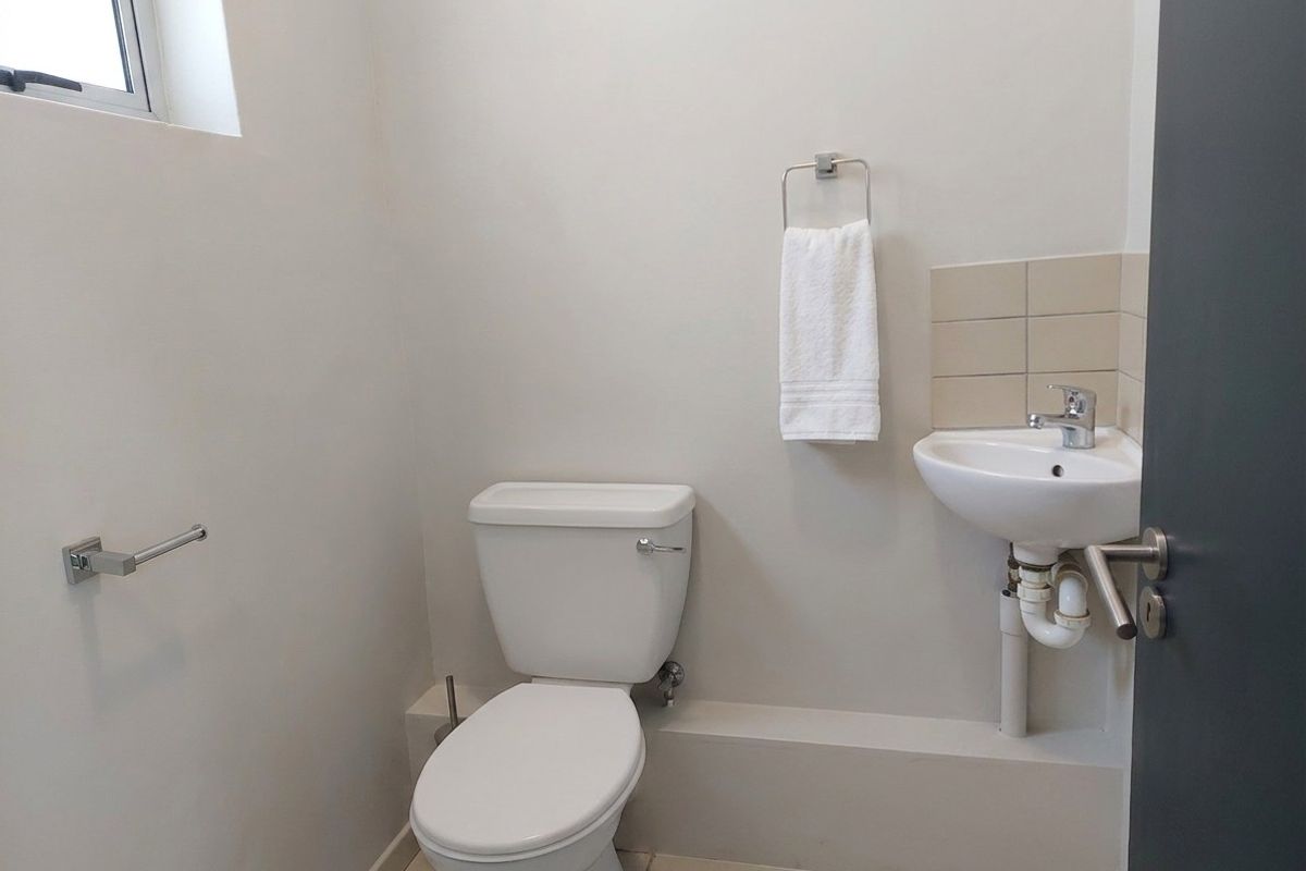 A compact, functional office restroom featuring a white toilet, wall-mounted basin with chrome fixtures, and neutral tiled flooring.
