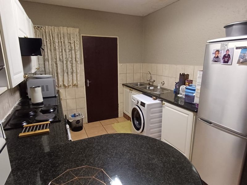 Functional kitchen featuring granite countertops, built-in cabinetry, a double sink, and an electric hob with tiled backsplash and flooring.