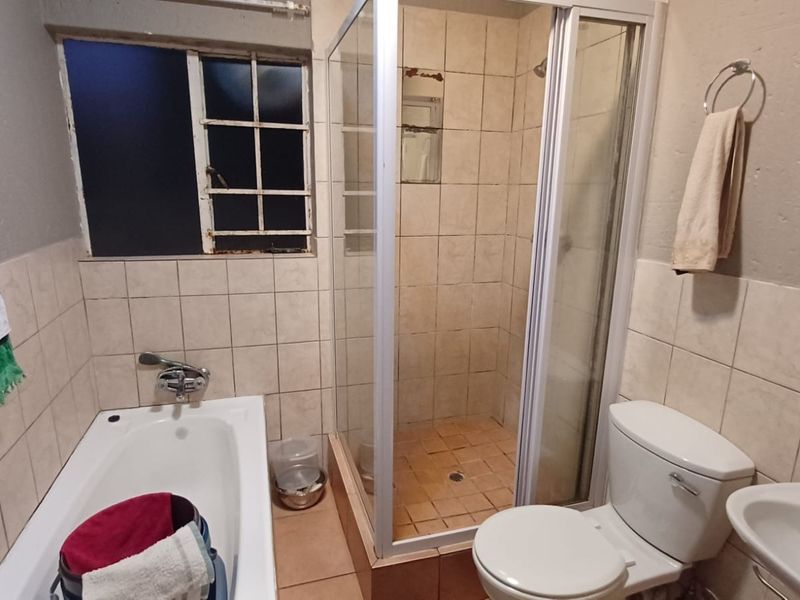 A functional bathroom featuring a bathtub, separate shower enclosure, toilet, and pedestal basin, with tiled finishes and a steel-framed window.