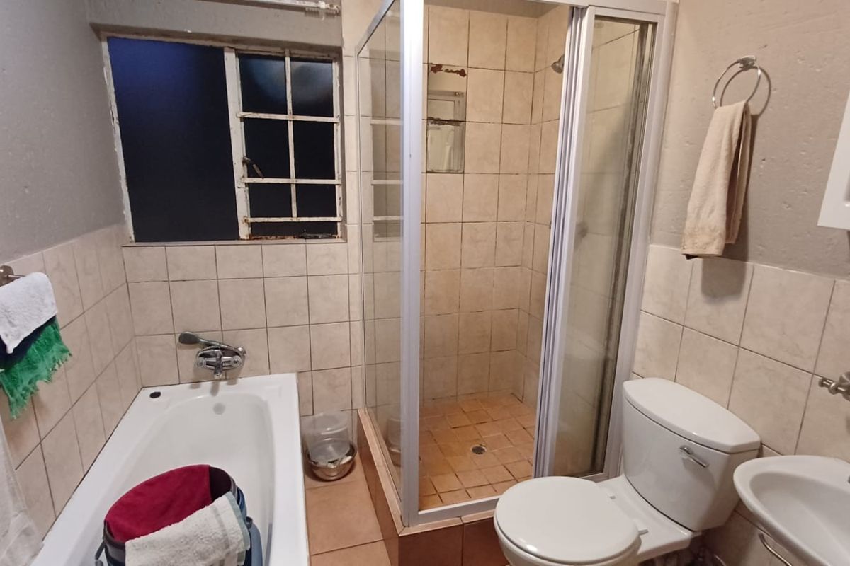 A functional bathroom featuring a bathtub, separate shower enclosure, toilet, and pedestal basin, with tiled finishes and a steel-framed window.