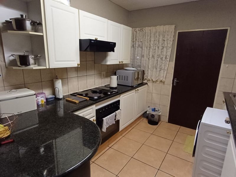 A functional kitchen featuring granite countertops, built-in oven with hob, extractor fan, and tiled finishes throughout.