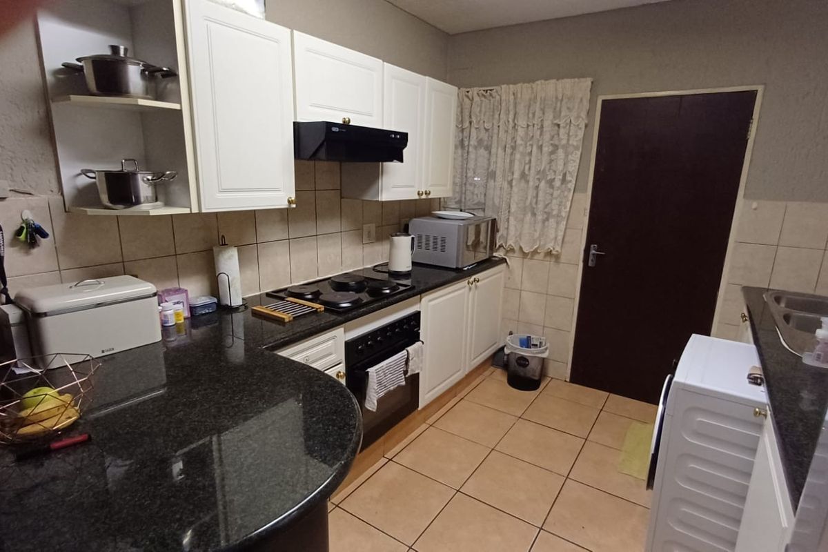 A functional kitchen featuring granite countertops, built-in oven with hob, extractor fan, and tiled finishes throughout.