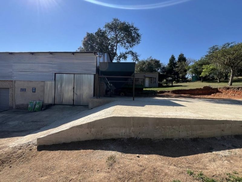 Exterior view of a farm utility building featuring a corrugated metal facade, large sliding doors, and a concrete loading ramp with an industrial hopper.
