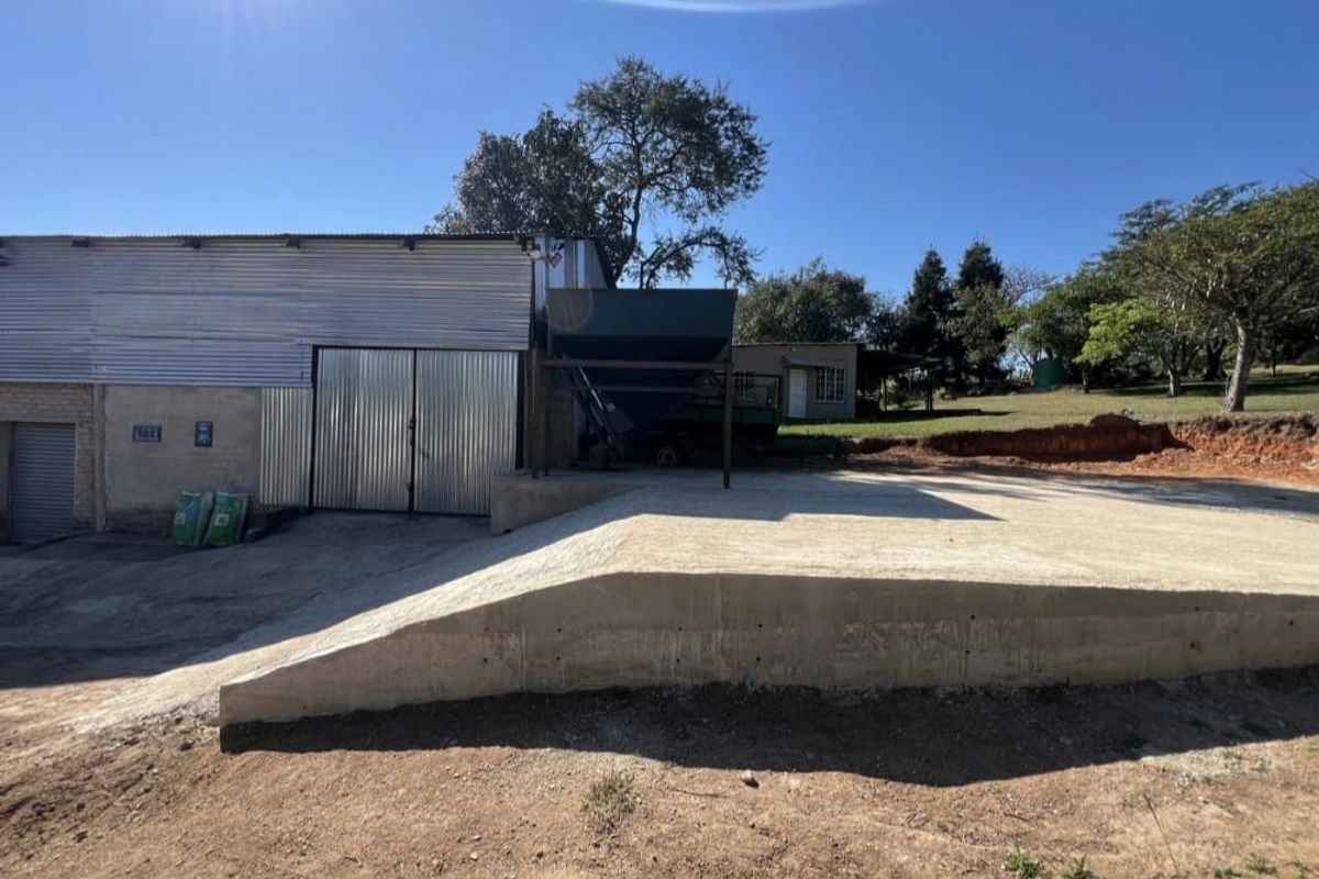 Exterior view of a farm utility building featuring a corrugated metal facade, large sliding doors, and a concrete loading ramp with an industrial hopper.
