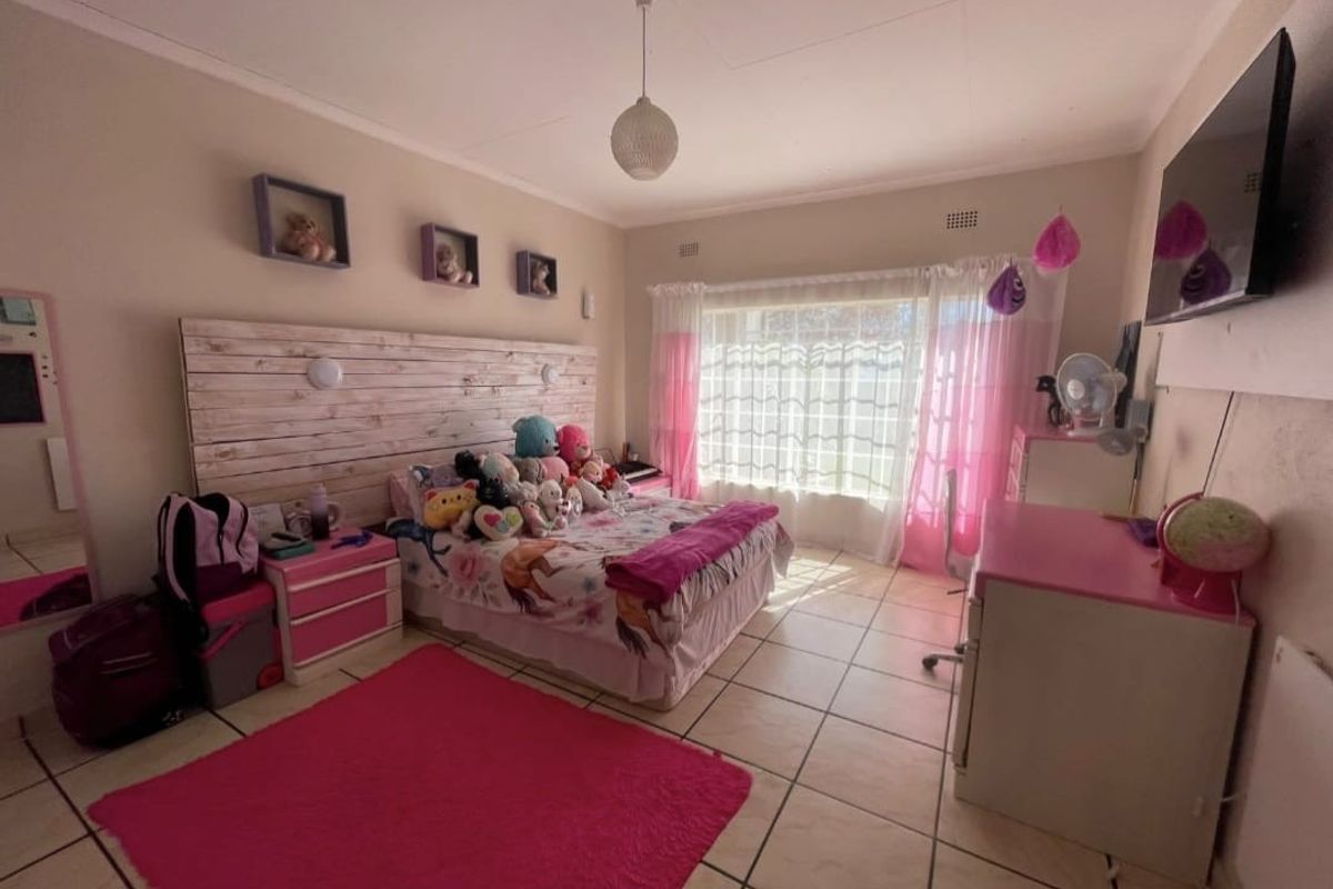 A spacious bedroom featuring tiled flooring, a built-in headboard, and a large window with security bars, providing ample natural light.