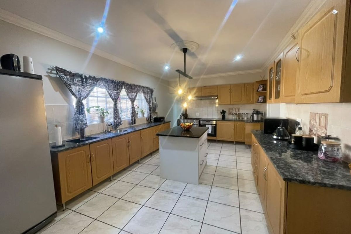 Spacious kitchen featuring light wood cabinetry, granite countertops, a central island, and ceramic tile flooring, offering a functional layout with ample storage space.