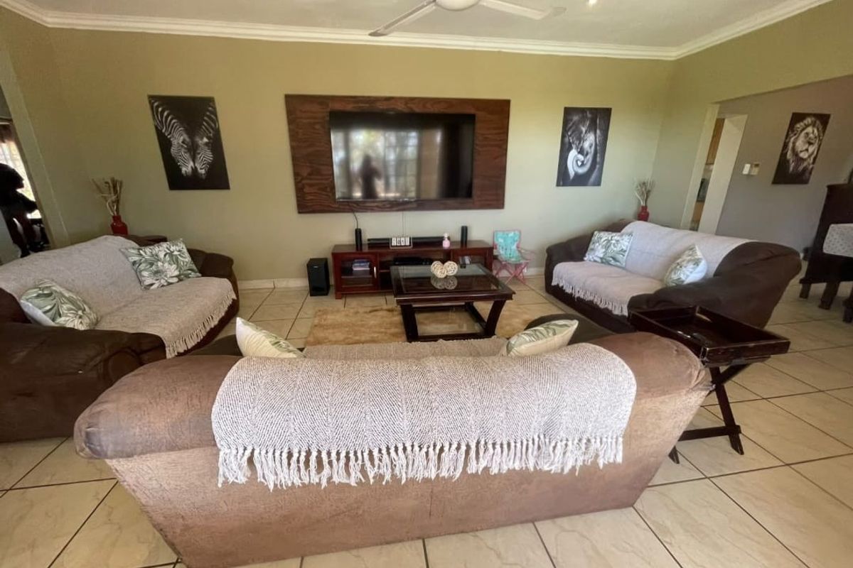 A spacious living room featuring tiled flooring, a ceiling fan, and a prominent built-in timber television surround.