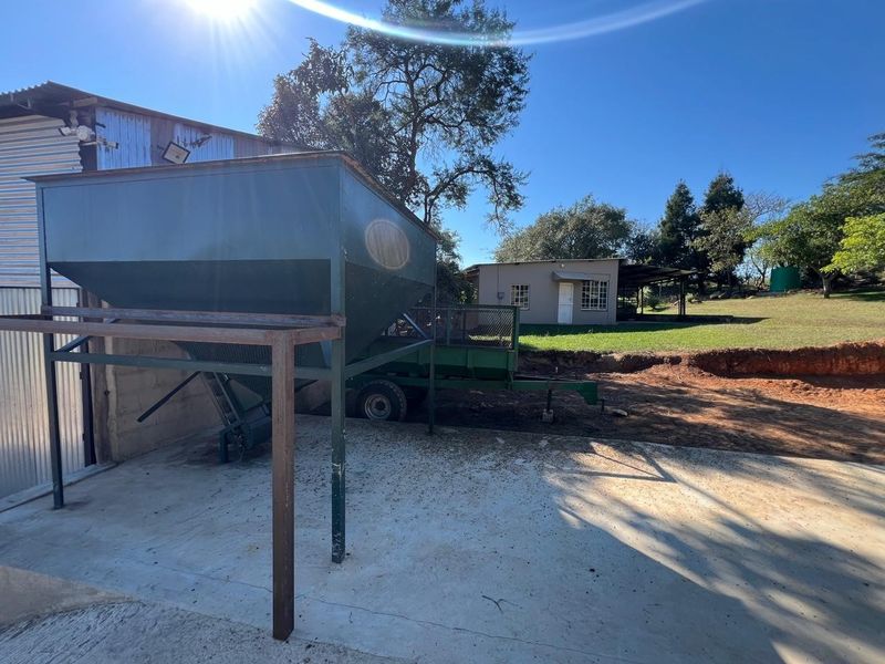 Rear farm yard area featuring a corrugated metal shed, a large grain silo, and an outbuilding set against a rural landscape.