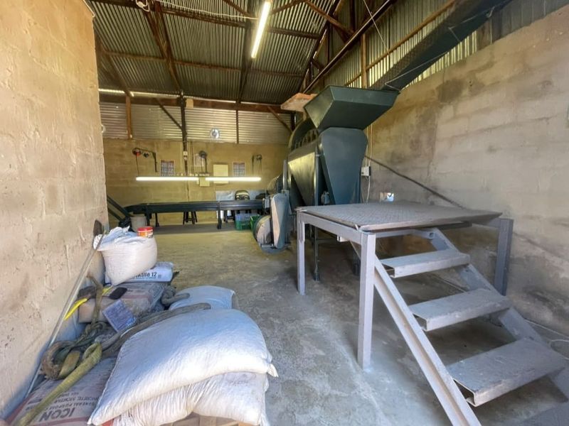 Functional farm utility space featuring concrete block walls, corrugated metal roofing, and industrial processing equipment installed on a concrete floor.