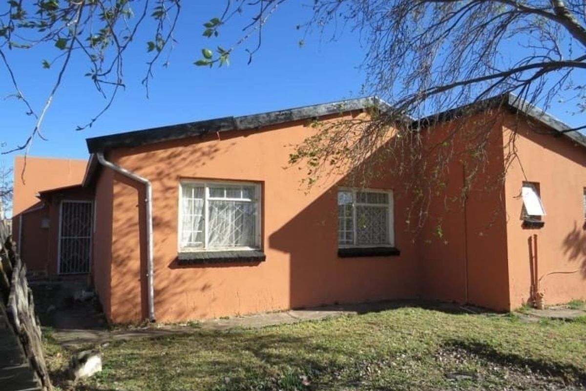 Rear exterior view of a single-story house featuring orange painted masonry walls, security bars on windows, and basic guttering systems.