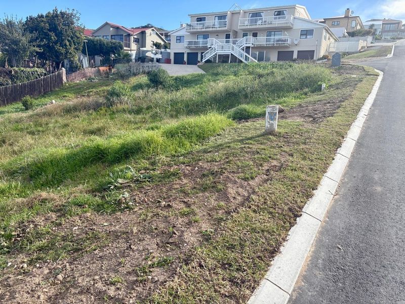 A vacant residential plot featuring a sloped landscape, concrete curbing, and a survey marker, situated in an established neighborhood.