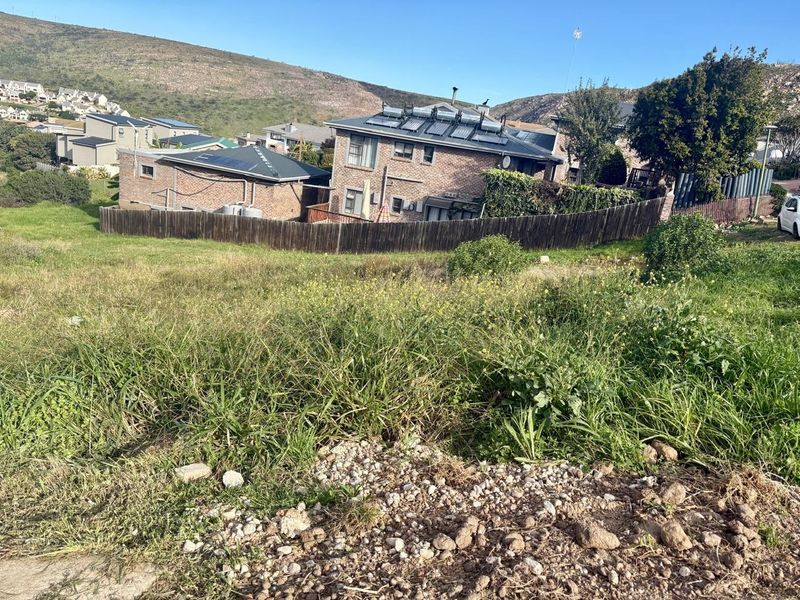 A view of a vacant residential plot featuring sloped terrain and existing perimeter fencing, situated in a developed neighbourhood.