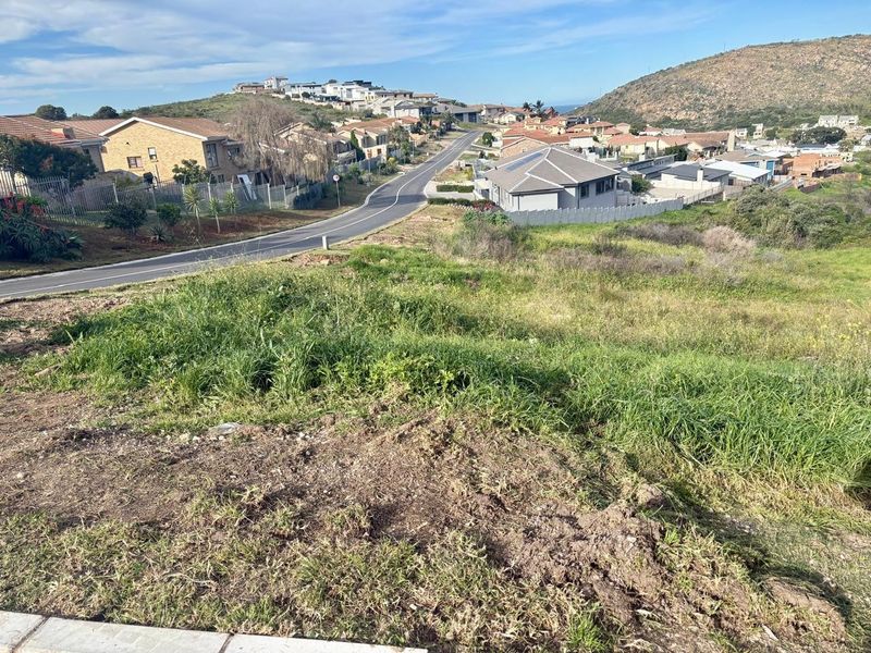 An elevated view overlooking a sloped residential plot with surrounding neighborhood infrastructure and distant hills.