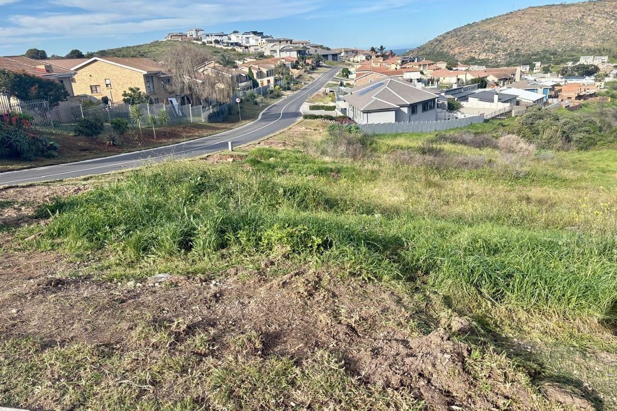An elevated view overlooking a sloped residential plot with surrounding neighborhood infrastructure and distant hills.