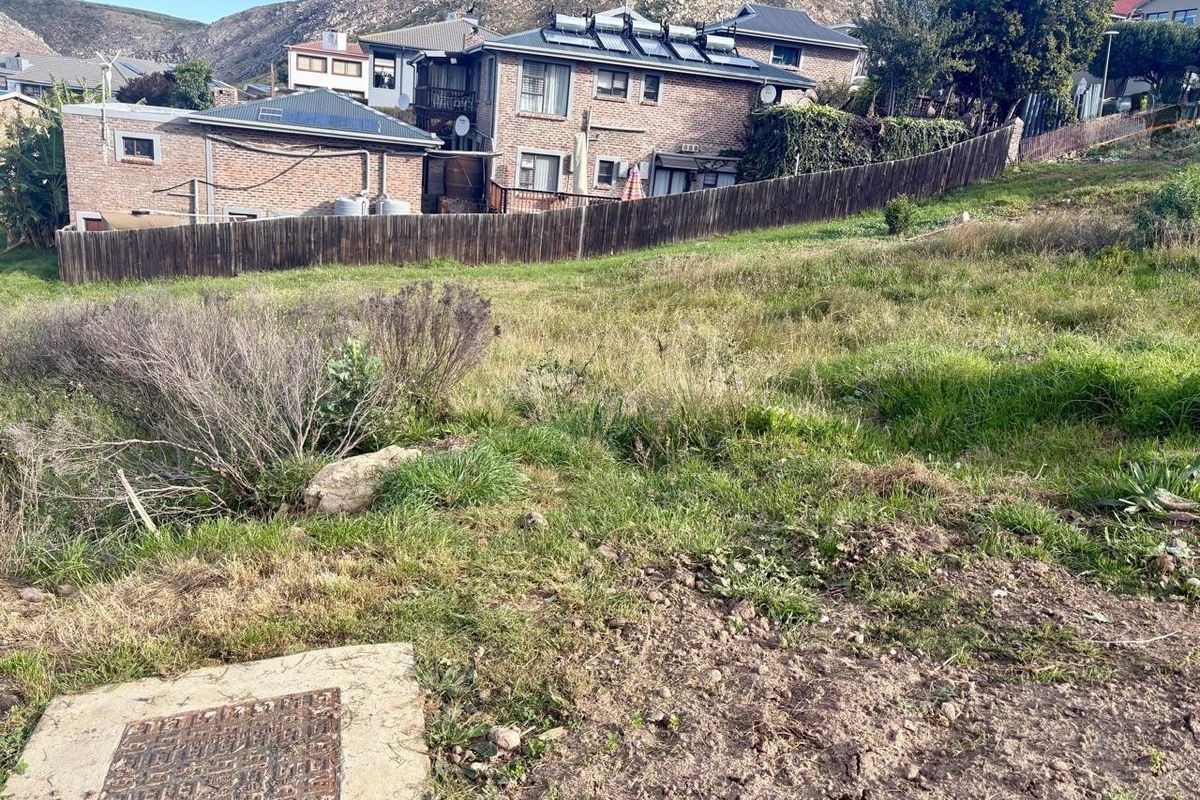 A view of a vacant residential plot featuring natural grass terrain, a timber boundary fence, and a visible manhole cover.