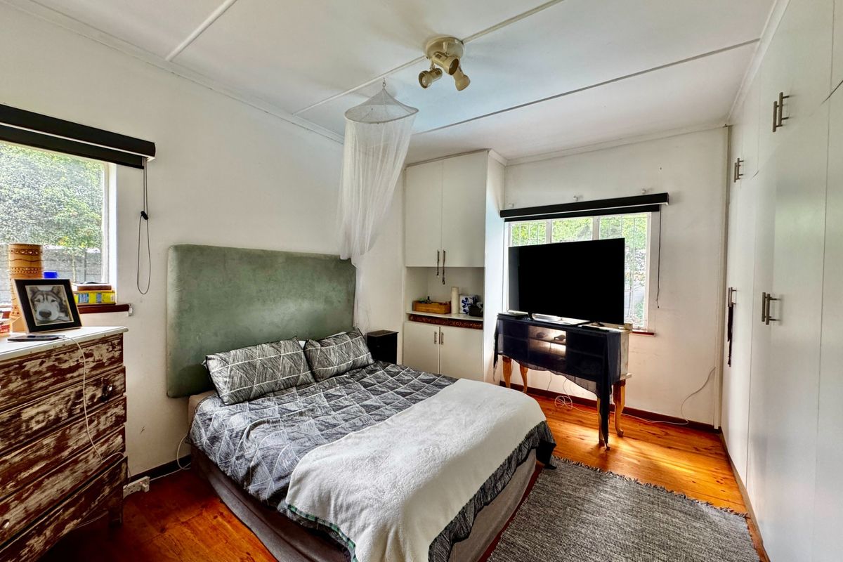 A bedroom featuring timber flooring, built-in cupboards, and natural light from dual windows.