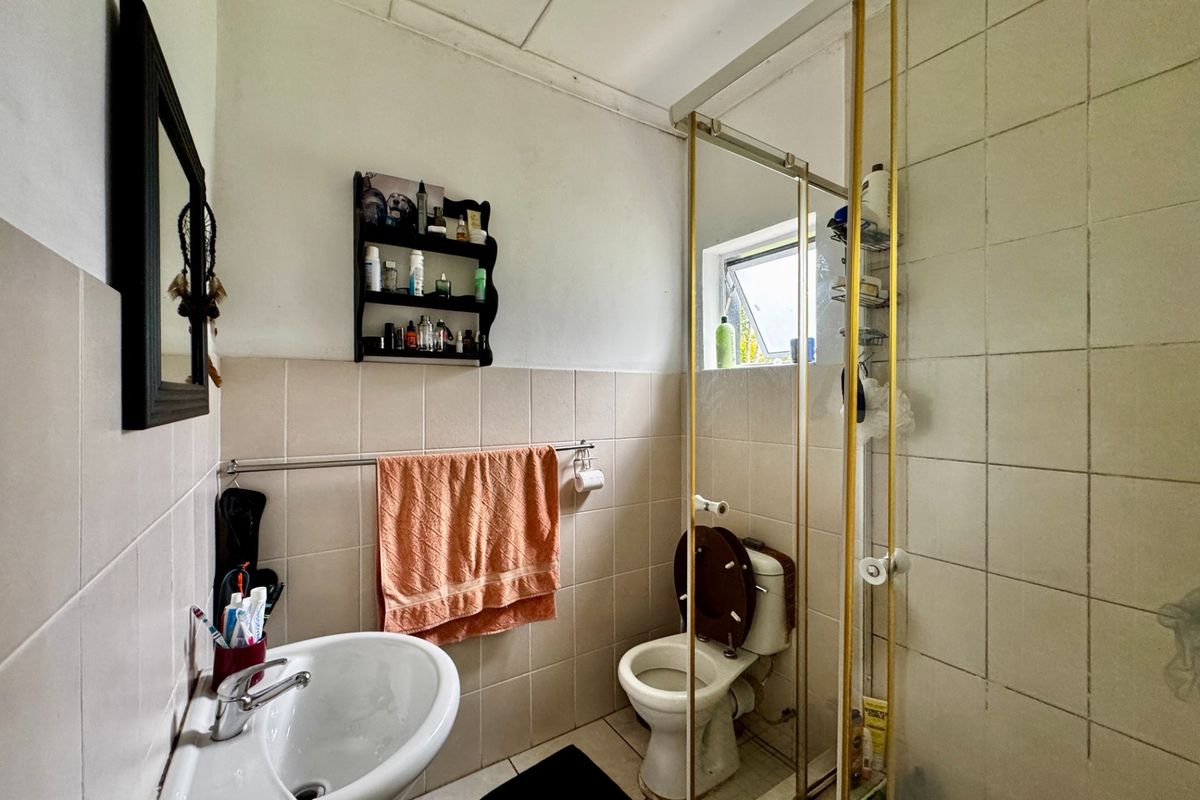 A compact bathroom featuring a pedestal basin, toilet, and a shower enclosure with tiled finishes, requiring some maintenance and cosmetic updates.