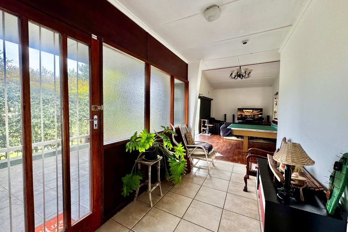 A spacious living area featuring tiled flooring, timber-framed glass doors, and wood paneling, offering a bright transition space leading into the main lounge area.