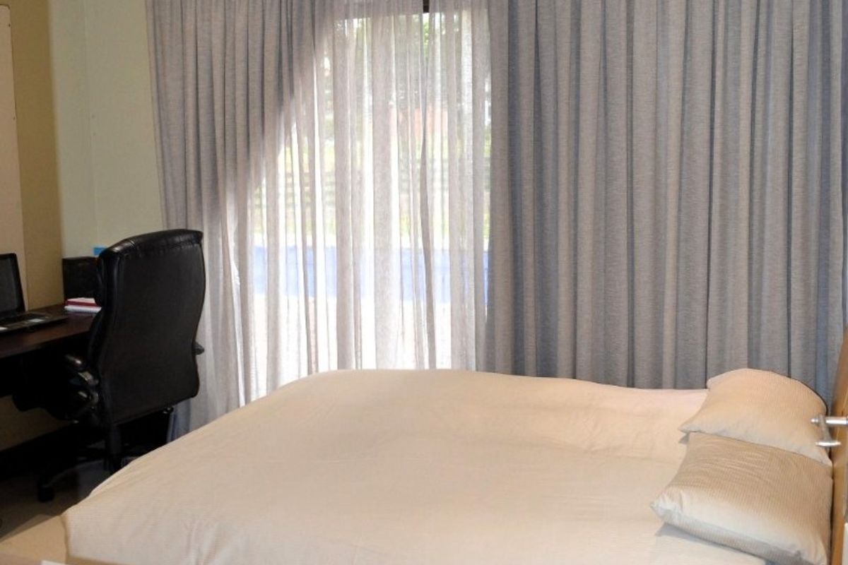A functional bedroom featuring tiled flooring, recessed downlights, and floor-to-ceiling curtains providing access to the exterior.