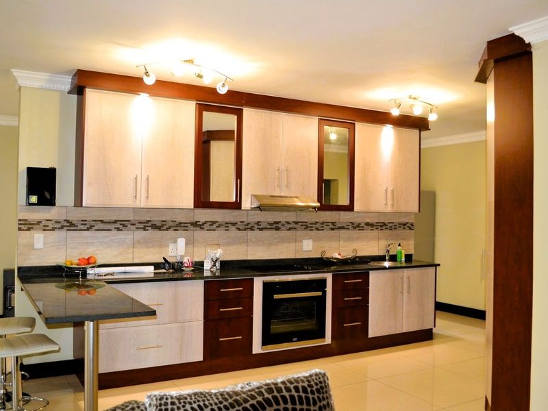 Modern kitchen featuring two-tone cabinetry, granite countertops, integrated oven, hob, extractor fan, and a convenient breakfast bar with tiled backsplash.