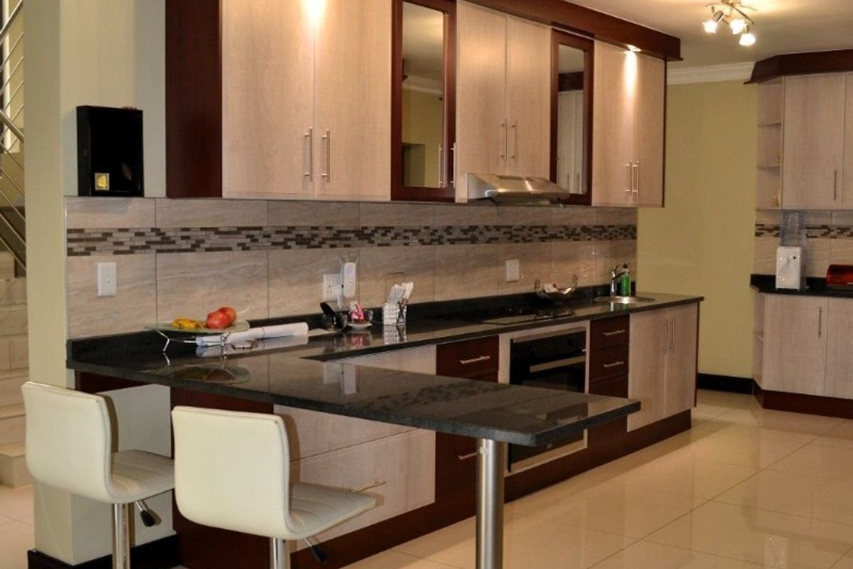 Modern kitchen featuring two-tone cabinetry, granite countertops, a breakfast bar, and integrated appliances with polished porcelain floor tiles.