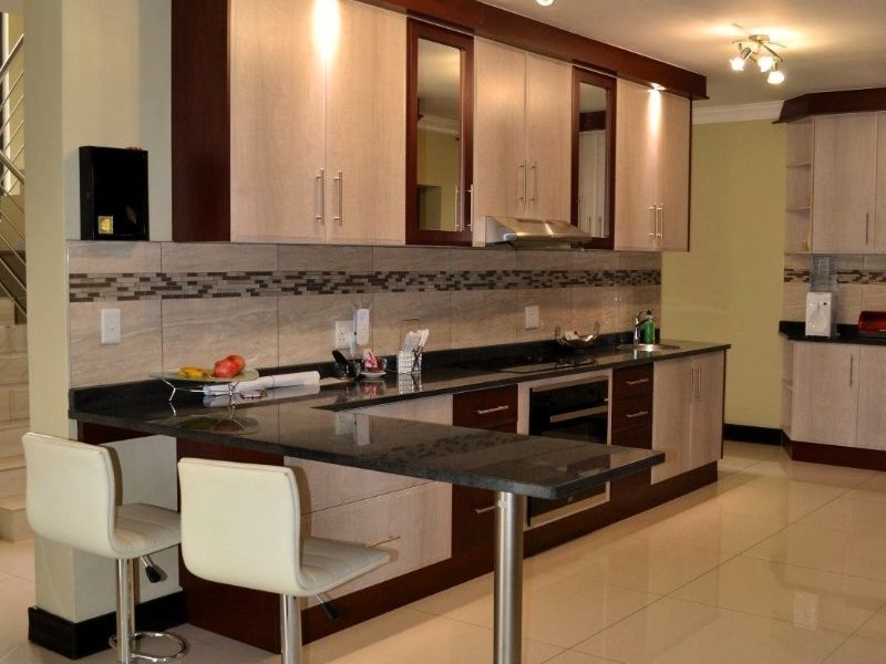 Modern kitchen featuring two-tone cabinetry, granite countertops, a breakfast bar, and integrated appliances with polished porcelain floor tiles.