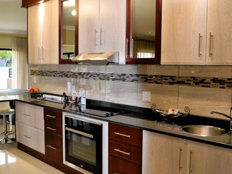 Modern kitchen featuring two-tone cabinetry, granite countertops, integrated stainless steel appliances, tiled backsplash, and polished porcelain flooring.