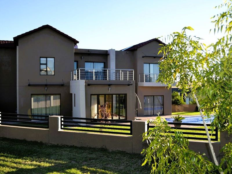 Rear view of a two-story residential property featuring a swimming pool, landscaped garden, and upper-level balconies with metal railings.