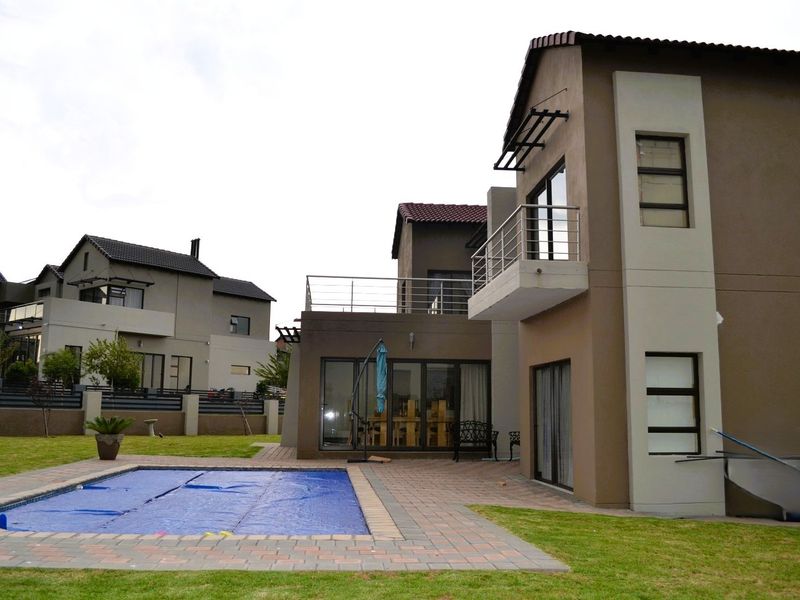 Rear view of a modern two-story house featuring a swimming pool, paved patio area, and an upper-level balcony with stainless steel railings.