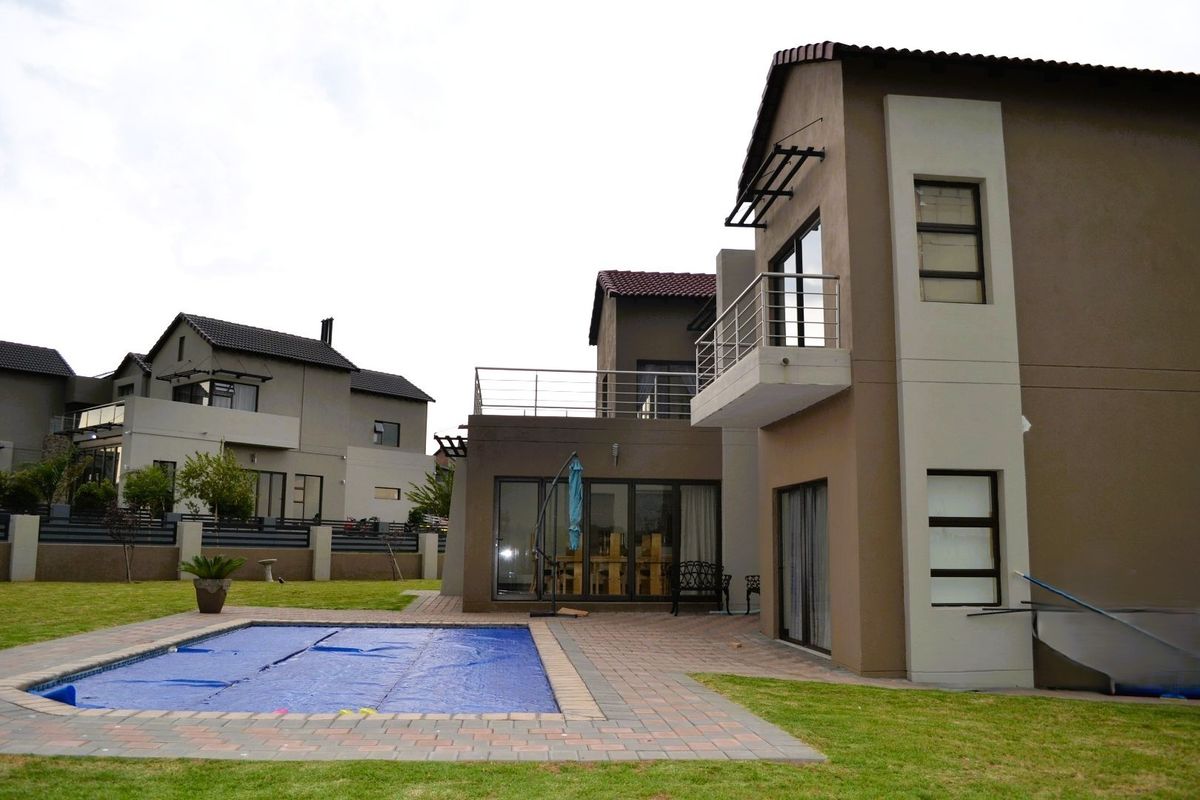 Rear view of a modern two-story house featuring a swimming pool, paved patio area, and an upper-level balcony with stainless steel railings.