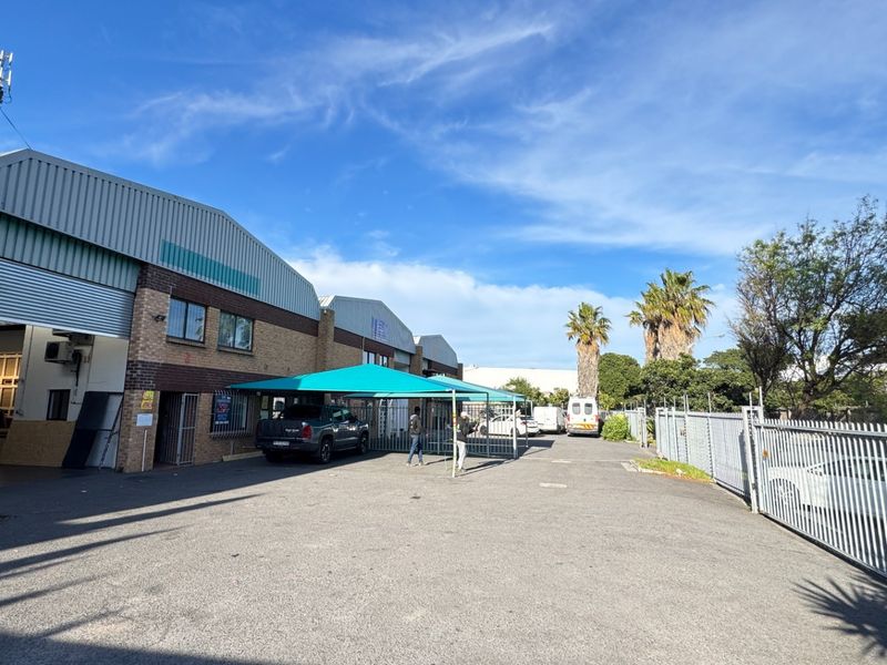 Industrial property exterior featuring a brick facade, roller shutter access, and a paved driveway with a shade cloth carport and secure perimeter fencing.