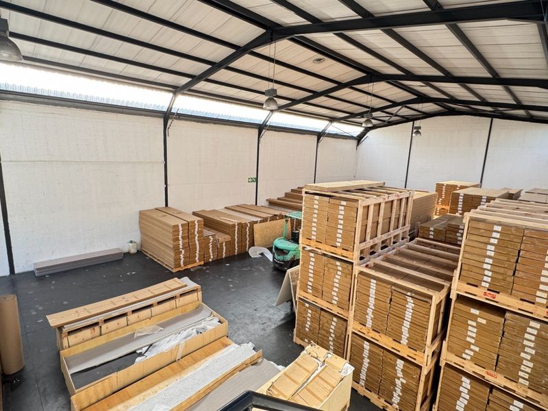 Spacious industrial warehouse unit featuring high ceilings with exposed steel trusses, concrete flooring, and ample natural light through translucent roof panels.