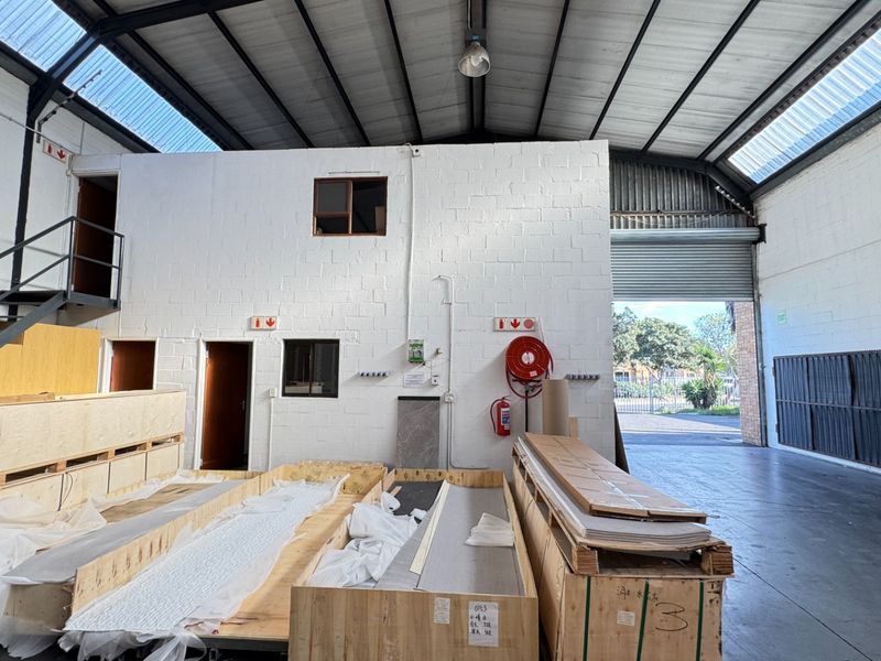 Spacious industrial warehouse unit featuring high ceilings with translucent roof panels, concrete flooring, a roller shutter door, and an integrated steel staircase.