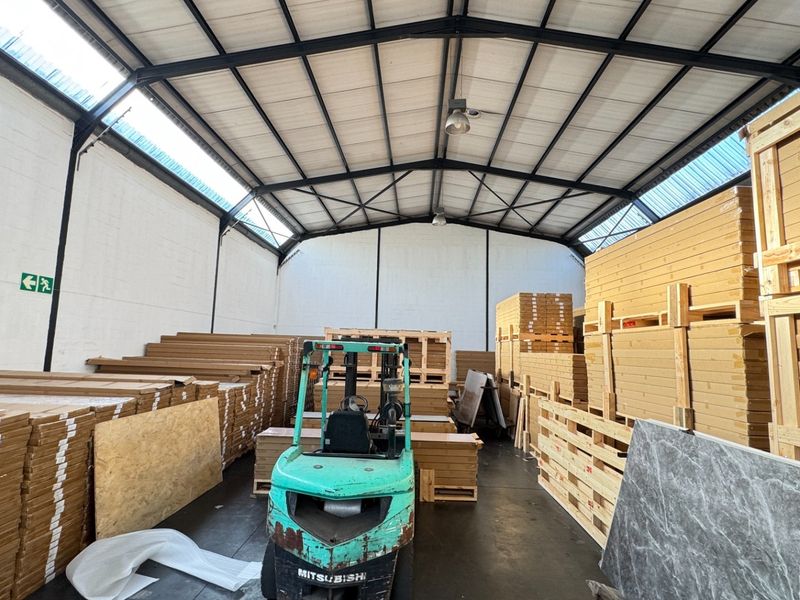 Spacious industrial warehouse unit featuring high ceilings with exposed steel trusses, translucent roof panels for natural light, and durable concrete flooring.