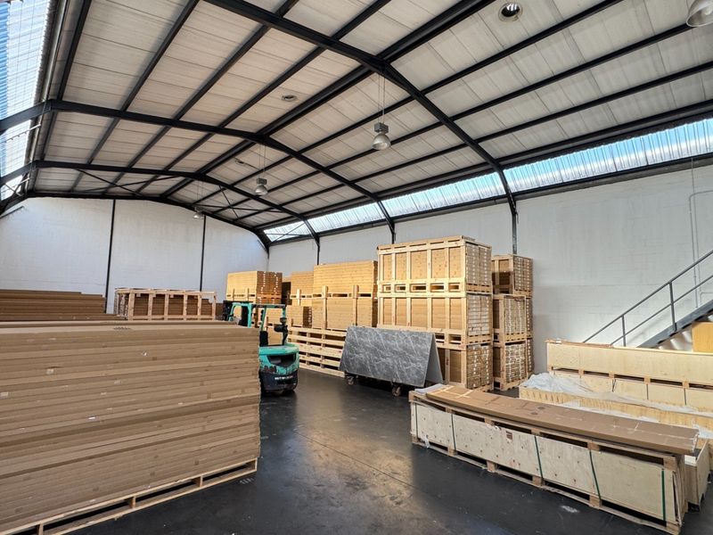 Spacious industrial warehouse unit featuring high ceilings with exposed steel trusses, translucent roof panels for natural light, and a functional metal staircase.