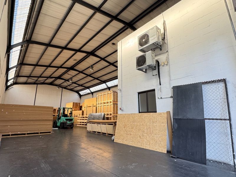 Spacious industrial warehouse unit featuring high exposed steel truss ceilings, durable concrete flooring, and wall-mounted air conditioning units.