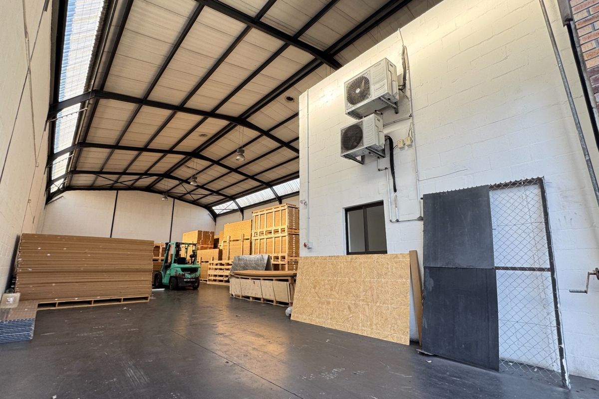 Spacious industrial warehouse unit featuring high exposed steel truss ceilings, durable concrete flooring, and wall-mounted air conditioning units.